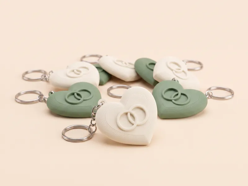 Llaveros de boda con forma de corazón impresos en 3D en marfil y verde salvia con dos alianzas en relieve, visual de ejemplo
