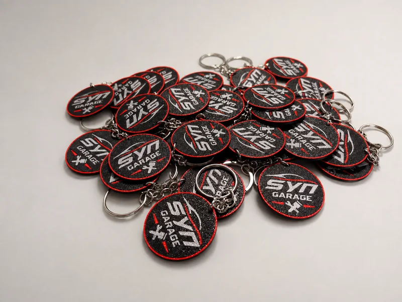 Serie de llaveros redondos personalizados en negro, rojo y plata con el logo de SYN Garage