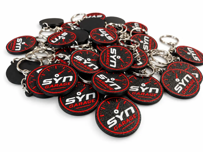 Segunda tirada de llaveros de SYN Garage con el diseño del cuentarrevoluciones en negro, rojo y blanco