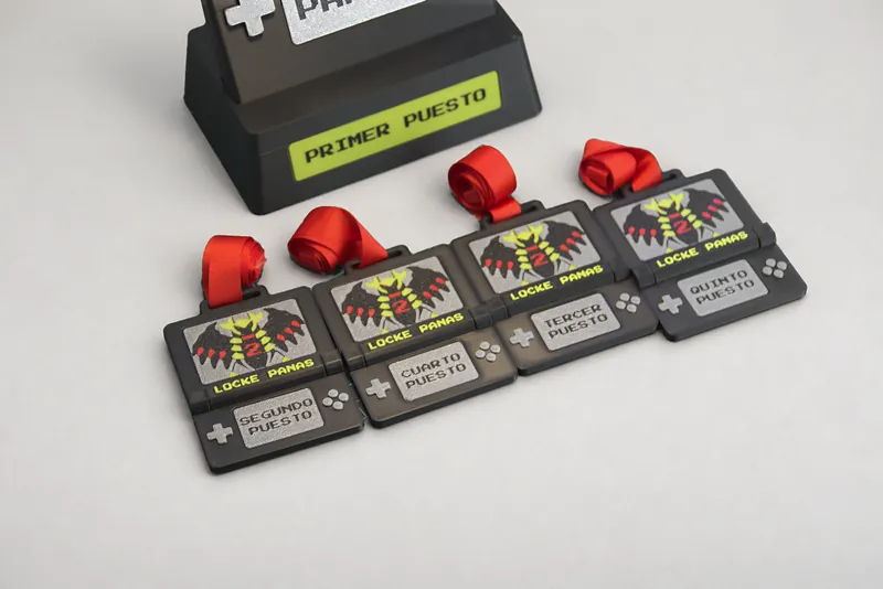 Cuatro medallas impresas en 3D con forma de consola portátil, del segundo al quinto puesto, con cinta roja