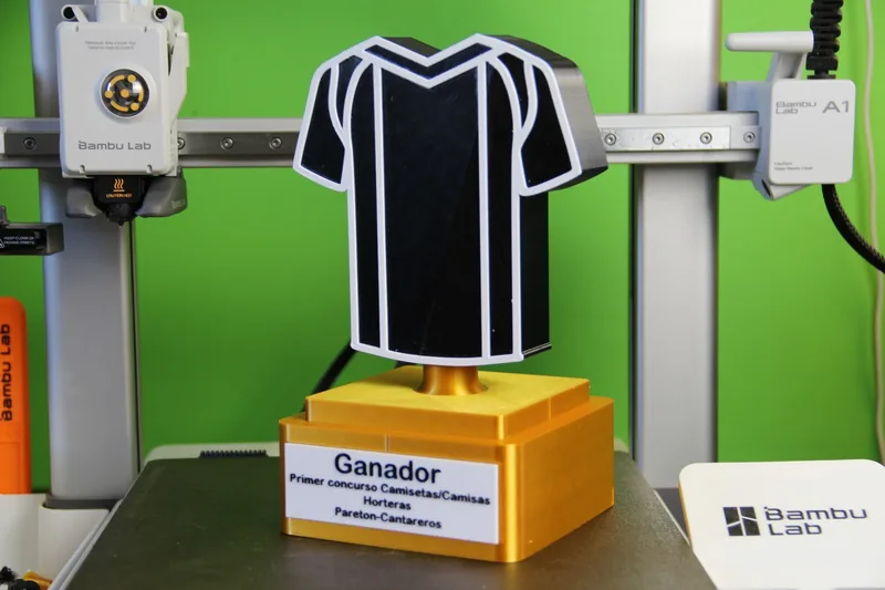 Trofeo personalizado recién impreso en 3D sobre la mesa del taller, junto a la impresora que lo ha fabricado