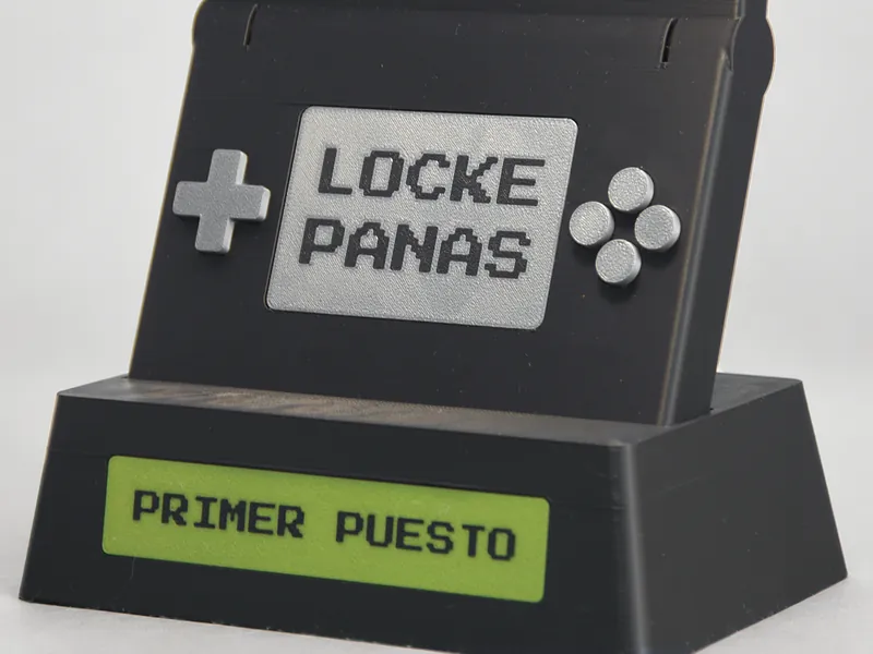 Trofeo de un torneo de videojuegos impreso en 3D con forma de consola portátil, el nombre del torneo en la pantalla y placa «PRIMER PUESTO»