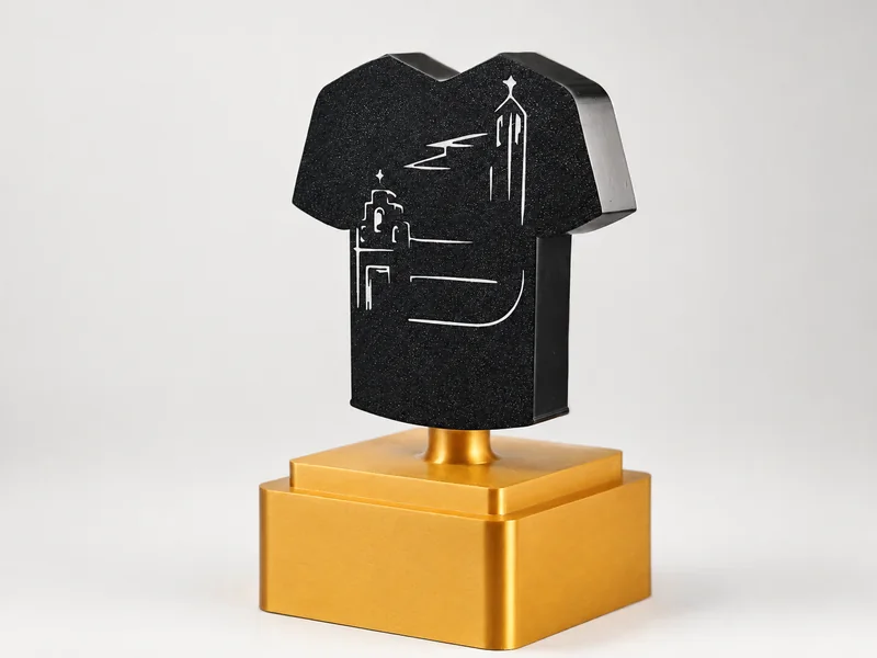 Trofeo personalizado con forma de camiseta negra, el perfil de una localidad en relieve y peana dorada
